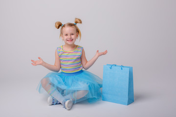 a little girl with a shopping bag sits on a skate Board on a white background
