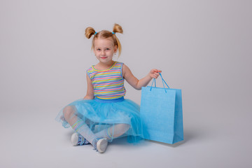 a little girl with a shopping bag sits on a skate Board on a white background
