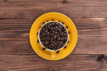 yellow cup filled with coffee beans on brown wooden boards. top view
