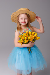 a little girl in a straw hat holding a yellow flower