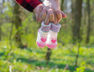 Couple holding hands, women holding baby shoes on fingers, close-up. Pregnant woman holding baby shoes.