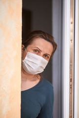 Coronavirus epidemic, home quarantine during the COVID-19 infection. Worried woman in a medical mask standing in the open doorway