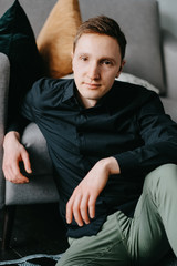 Obraz premium Handsome young man sitting on the floor near the sofa at home