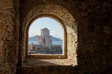 Methoni Castle in sunny weather during early morning with water waves in Greece viewed from a stone arch window