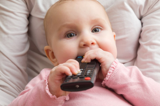 Infant sitting in mother lap and chewing remote control. Closeup. Front view. Favourite baby thing.