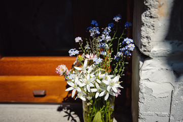 Fototapeta na wymiar A beautiful bouquet of flowers in a glass vase on the windowsill of the old house. White and blue forest flowers in the sun