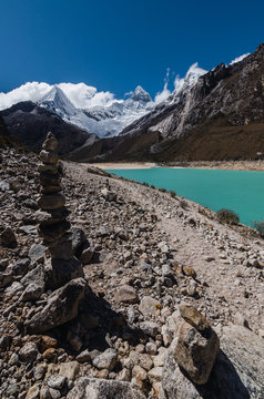 .piling of stones and trekking path in the turquoise lagoon of paron and with snowy high mountain peaks in the background, peru