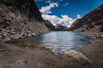 paron glacier lagoon flanked by rock walls and high pyramid mountain in the background covered in ice and snow, peru