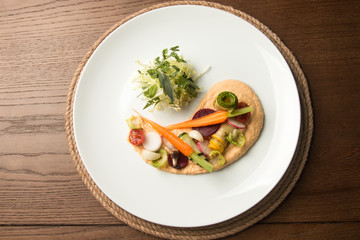 An interesting serving of vegetables on a plate on a wooden background. Very tasty food, healthy food, lunch in a restaurant, upper class, salad