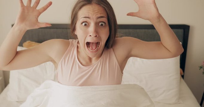 Young woman looking worried and stand up fast while oversleep. Panicing pretty girl realising late wake up for work while sleeping on bed. Concept of people and lifestyle.