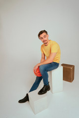 Modelo sentado en estudio con balon de baloncesto camiseta amarilla y vaquero