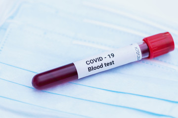 Vacuum tube with blood test identified by the COVID-19 coronavirus on white background. Protective medical mask and a tube