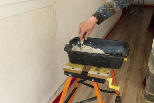 D&eacute;pose d'enduit, de pl&acirc;tre sur un mur par un pl&acirc;trier et pr&eacute;paration du m&eacute;lange dans une auge pour boucher et lisser l'enduit sur la paroi &agrave; l'aide d'un couteau et d'une spatule