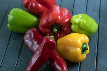 Composition of peppers of three different colors. Bright colors of vegetables. Juicy fresh peppers on a dark wooden table. Red, yellow, and green.