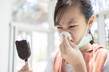 Sick asian child girl has runny nose and blows her nose into a tissue paper while eating too much...