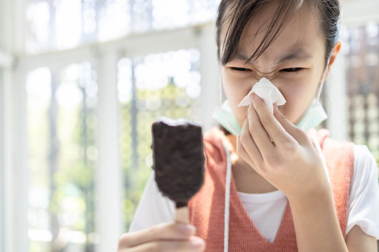 Sick asian child girl has runny nose and blows her nose into a tissue paper while eating too much ice cream,woman with illness from colds,sneeze,influenza,symptoms of infection,respiratory problems.