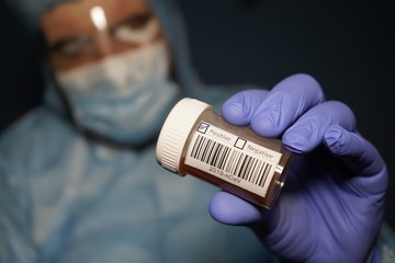 A doctor in a protective medical suit holds a flask with Covid-19 tests. Test result 