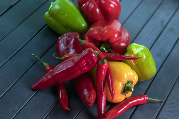 Composition of peppers of three different colors. Bright colors of vegetables. Juicy fresh peppers on a dark wooden table. Red, yellow, and green.