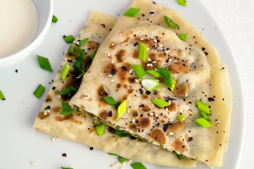 qutab with spinach and cheese decorated with green onion, sumac and sesame seeds and served with yogurt