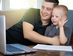 Father and son are talking via video link with relatives or teacher. The concept of online communication through the Internet and a video camera in a laptop. A call to grandparents during quarantine