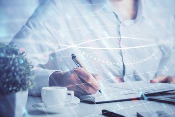 Double exposure of man's hands writing notes of stock market with forex chart.