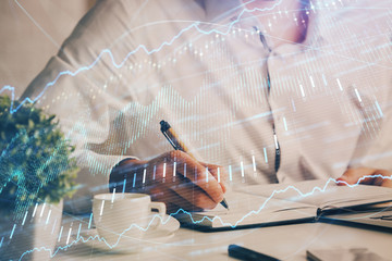 Double exposure of man's hands writing notes of stock market with forex chart.