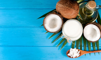 .coconuts, coconut oil and leafing palm trees on blue wooden background