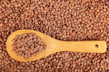Grains of lentils with a wooden spoon as a background