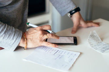 Woman making a shopping list in the kitchen trying to save money and checking tickets
