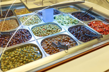 different color and taste olives in the marinade, on the counter in the store