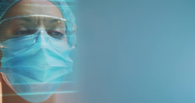 Female doctor with surgical mask swiping holographic screen for studying medical records. Shot on a blue background.