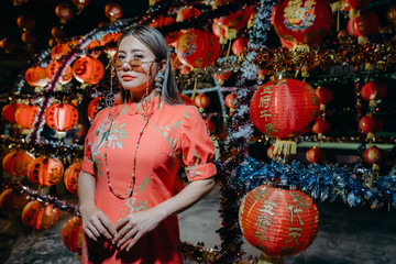 A beautiful asian woman on modern Chinese traditional dress standing at front of red lantern for Chinese new year.