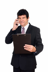 Mature handsome businessman talking on the phone while reading on clipboard