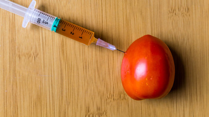 Injection syringe in raw tomato, concept of injection of GMOs
