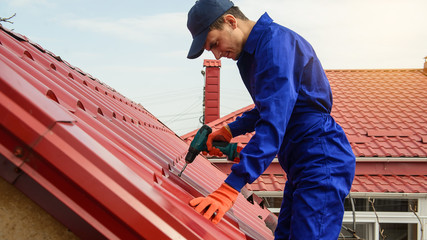 Young man worker in blue overall fix a metal tile roof