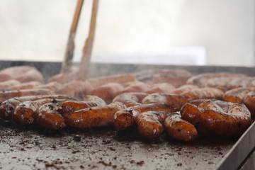 Sausages sizzling on a barbecue with a pair of tongs in the background at a local street fair