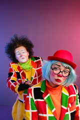 Two clowns a man and a woman with makeup in bright colored costumes are fooling around and showing a presentation