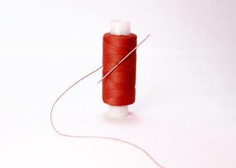 Spool of red thread with needle on white background