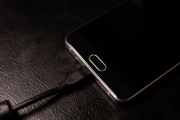 Black smartphone is charging on black table