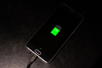 Black phone is charging with cable, green battery, on black table