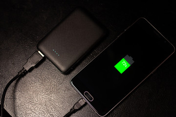 Black smartphone is charging from power bank on black table