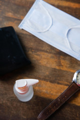 Essential item during restriction movement order lockdown concept. Mask, sanitizer bottle, wallet & watch on top of brown wooden table.