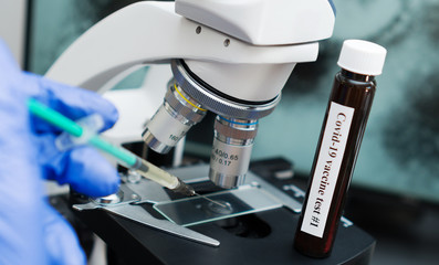 Virologist's hand in glove testing coronavirus vaccine under microscope.