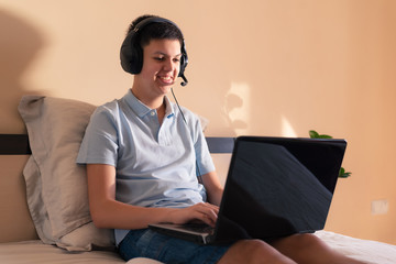 Happy teenage boy in headphones in front of laptop on distance learning. Smiling student learning language online. E-learning and study support concept. Staying home during quarantine.