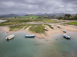Small fishing boats at low tide on the Escudo river and the surrounding marsh land, in San Vicente de la Barquera, Cantabria, Spain