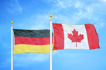 Germany and Canada two flags on flagpoles and blue cloudy sky