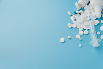 scattered variety pills, drugs, spay, bottles, thermometer, syringe and empty shopping trolley cart on blue background. pharmacy shopping concept