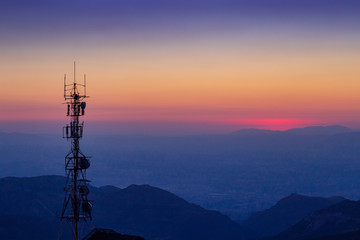 Antena de telecomunicaciones a contraluz con paisaje de montañas en el fondo al anochecer
