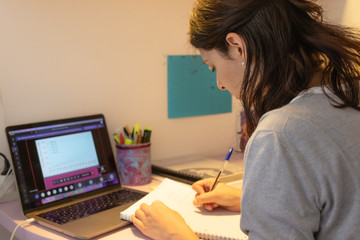 young brunette caucasian girl attending an online medicine class in her bedroom and taking notes, concept of social distancing, school at home