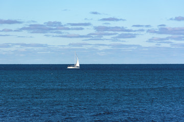 Obraz premium A sailboat cruises on boundless seas. A white sailboat on a blue sea. Classic blue color of the sea